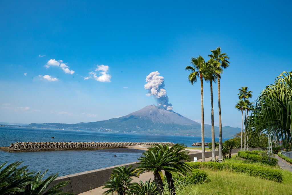 桜島の山頂から噴煙が立ち上る様子。2025年の噴火で火口から3000メートルに達した煙と、周囲に広がる火山灰の景観を示す。